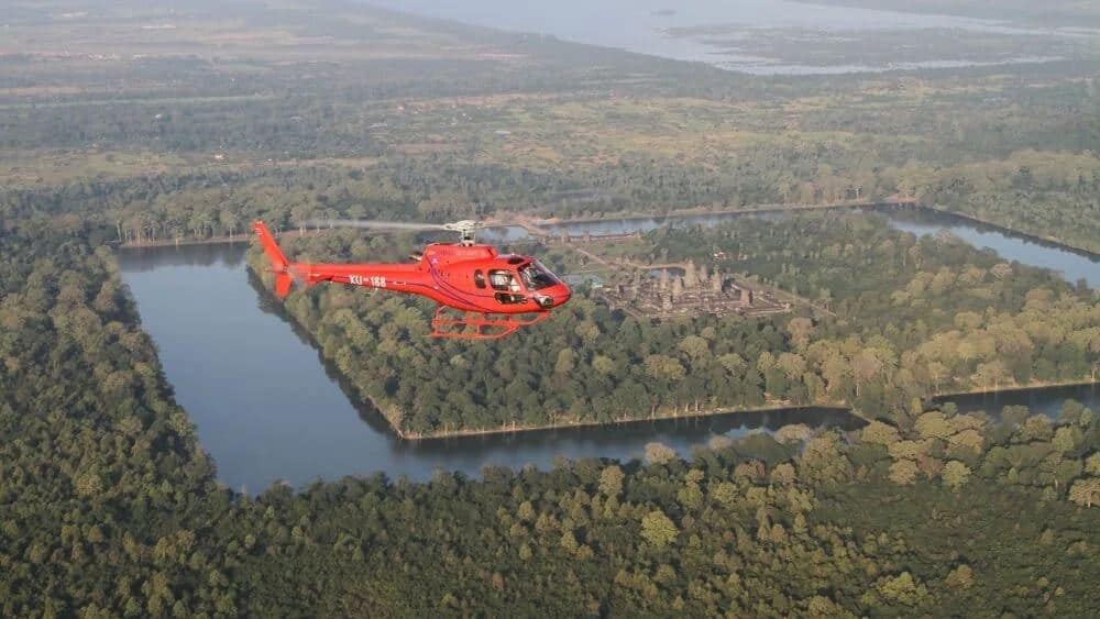 Red helicopter flying over forest