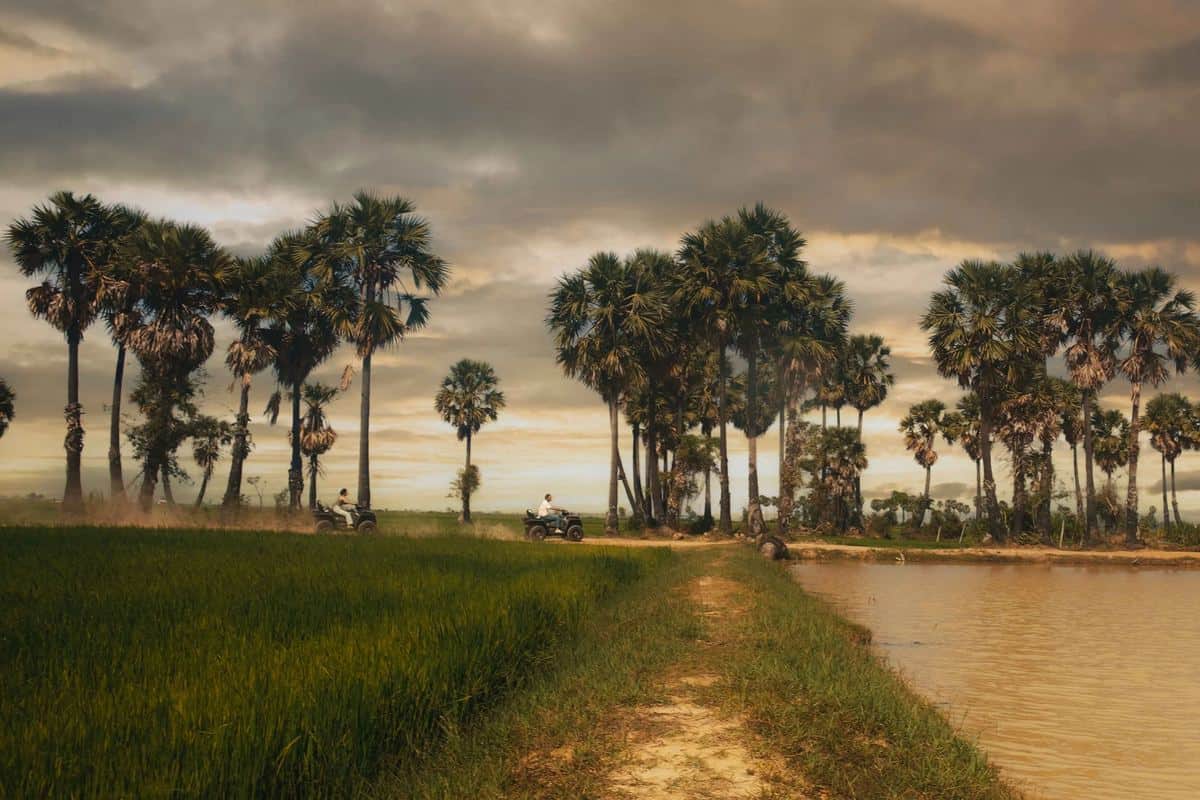 Two people on ATVs by a river at sunset