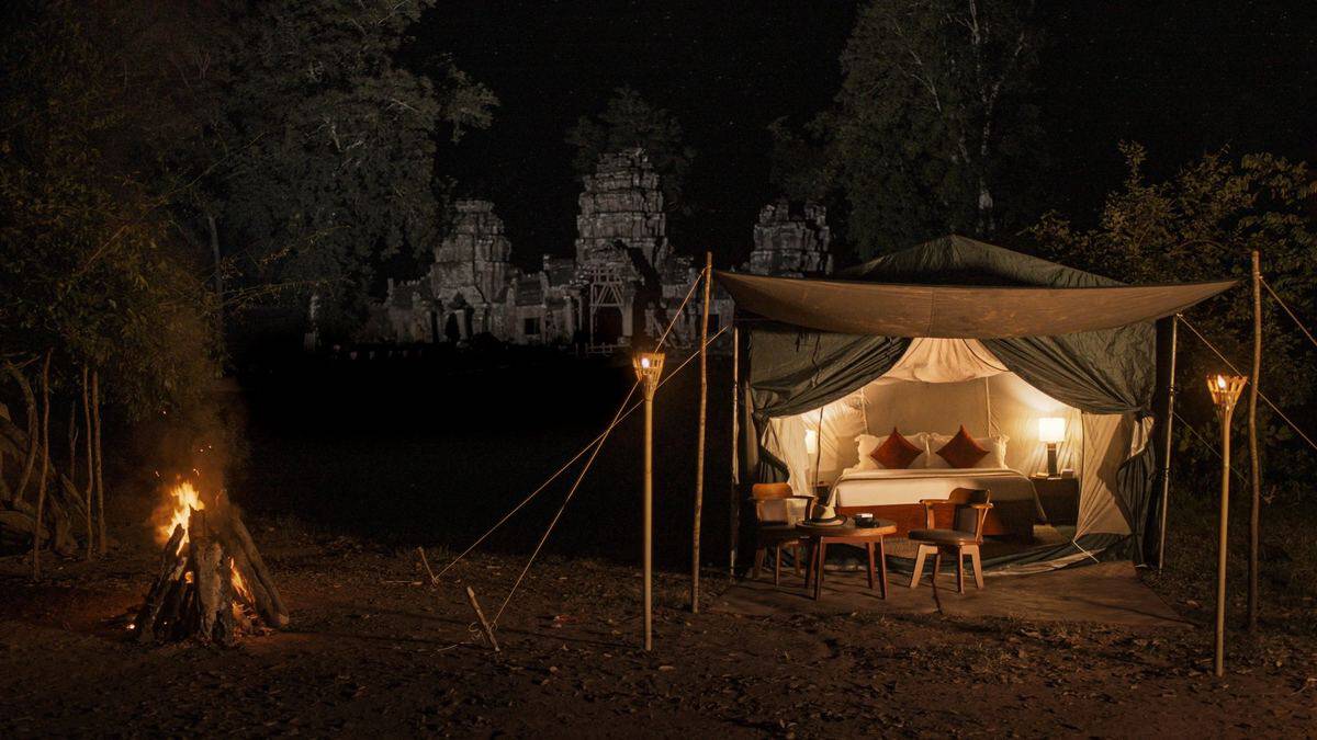 Luxury glamping tent in a forest at night with temple ruins behind