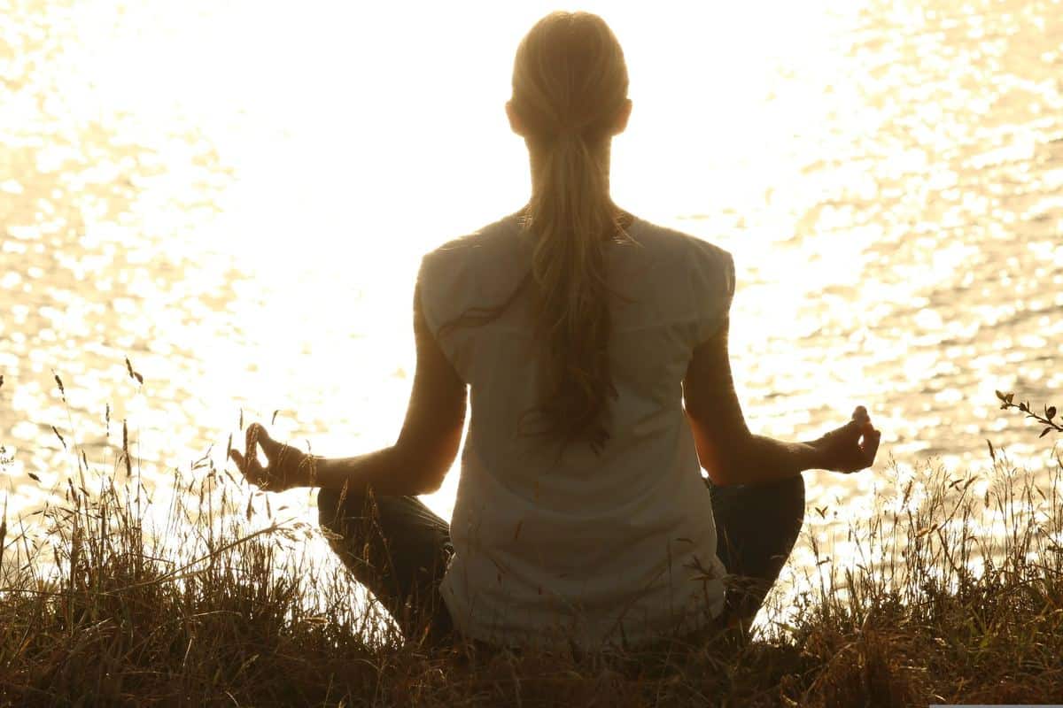 Woman meditating by water at sunset